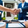 Buyer and seller shaking hands in front of a house, surrounded by real estate agents and paperwork