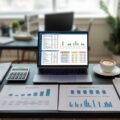 A workspace with a laptop, calculator, documents, and charts showing real estate expense analysis on a desk.