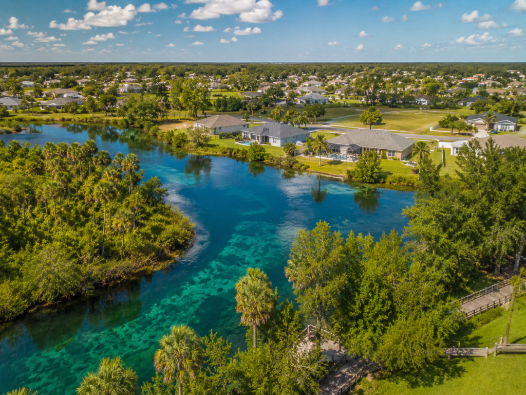 Single family homes along the lake in North Point Florida with a subdivision of homes in the background on a bright and sunny day