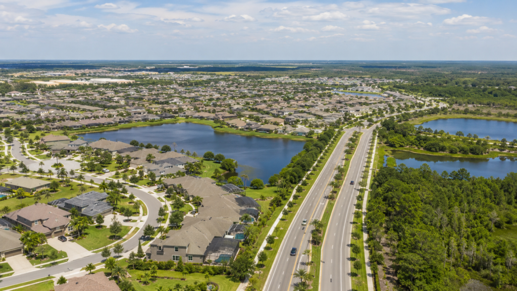 Aerial view of Pasco County suburban neighborhoods with lakes, green space, wide roads, and residential development.