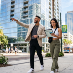 A stylish Gen Z male real estate investor and his girlfriend walking through the sun-drenched streets of downtown Tampa. The man, dressed in contemporary smart-casual attire, points toward a modern glass high-rise building while his girlfriend observes a digital tablet showing property details. The surrounding urban landscape features palm-lined sidewalks, sleek coastal architecture, and the bright, clear light of a Florida afternoon reflecting off the glass facades of nearby skyscrapers.
